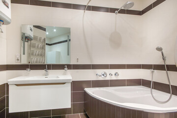 Bathroom with modern design. The finish is made of beige and brown tiles. Corner bath with shower.