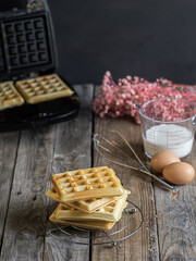freshly made homemade waffles on a rack, ingredients on the side and waffle iron on the bottom....