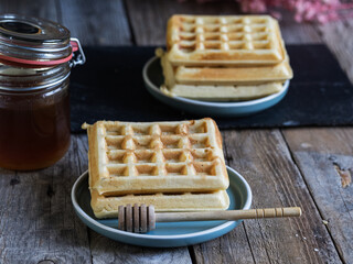 Homemade waffles with honey jar on a wooden table. Warm and minimal breakfast composition in a rustic kitchen setting.