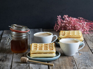 Homemade waffles with coffee and honey jar on a wooden table. Warm and minimal breakfast composition in a rustic kitchen setting.