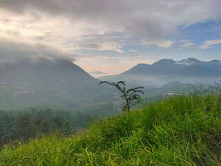 Morning clouds cover the lush green mountains under the sky, mountain view from the top of the hill in the morning