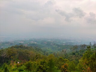 Misty hills meet the distant cityscape, blending nature's calm with urban sprawl beneath soft clouds