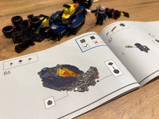 Naklejka premium Moscow, Russia, April 26, 2025: LEGO Speed Champions Red Bull Racing Formula 1 car partially assembled, shown next to step by step instructions and scattered LEGO parts on a wooden surface