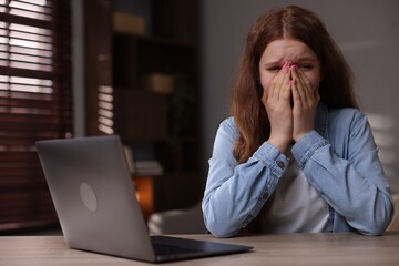 Sad teenage girl with laptop at table indoors
