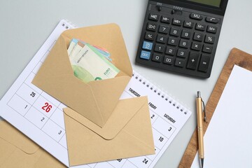 Money bonus. Envelopes with euro banknotes, calculator and calendar on light grey background, flat lay