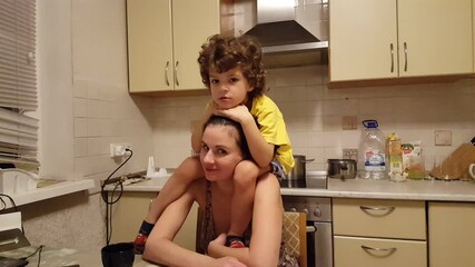 Son sits on the shoulders of his mom, playing and smiling joyfully.