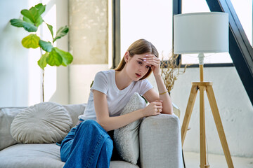 Sad teenage girl 17-18 years old sitting at home on the couch