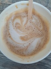 Fresh cappuccino in a paper cup with foam art and bubbles, photographed from above