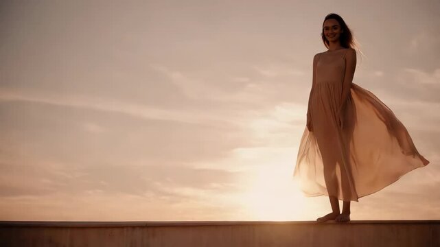 Frau im Wind bei Sonnenuntergang im Urlaub auf einer Mauer am Meer.