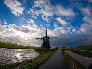 An ancient Dutch windmill used for pumping water on a blue sky with white clouds. Amazing landscape from the Netherlands at dusk in spring time 