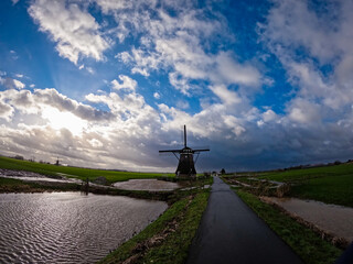 An ancient Dutch windmill used for pumping water on a blue sky with white clouds. Amazing landscape from the Netherlands at dusk in spring time 