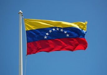 Venezuelan flag waving against a clear blue sky, symbol of national identity
