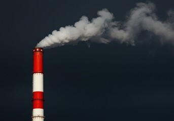 Red and white industrial chimney with smoke against a dark sky