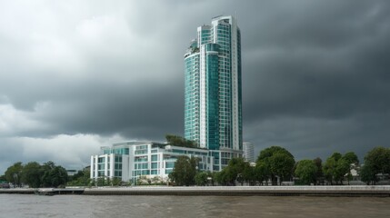Modern Glass Tower Against Dramatic Cloudy Sky Over Water Landscape
