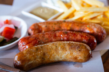 Close-up of grilled sausages served with crispy French fries, mustard sauce, and pickled vegetables. Juicy and flavorful meal perfect for food advertising, menu design, and restaurant promotions.