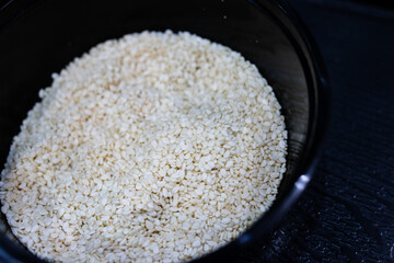 Close-up of white sesame seeds in a black bowl on a dark surface. A healthy ingredient used in Asian cuisine, baking, and seasoning. Ideal for food backgrounds and nutrition concepts.