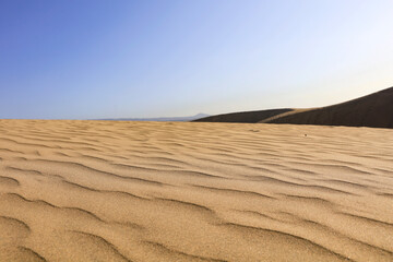 Hot, sunlit sand with natural wavy patterns resembling small dunes on wild, untouched beach. Calm...