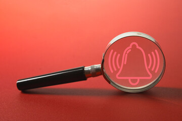Magnifying glass focusing on a ringing alarm bell icon on a vibrant red background. Concept of urgent notification, important reminder, alert system, attention signal, or breaking news.
