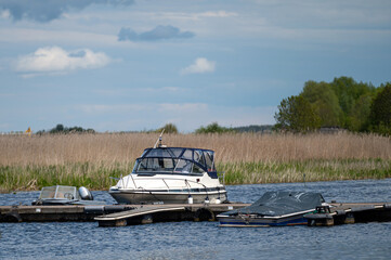 Boats docked on a calm lake surrounded by lush greenery and clear skies