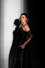 Elegant model poses in a stunning black dress with intricate lace sleeves against a contrasting light backdrop