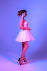 Fashion model poses elegantly in a shimmering white dress against a vibrant purple backdrop during a studio photoshoot