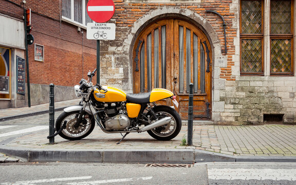 Yellow classic motorcycle parked on sidewalk in old town. Side view of Triumph Thruxton 900 bike on the street in central Brussels near 16th century Bruegel House. Brussels, Belgium - October 09 2014.