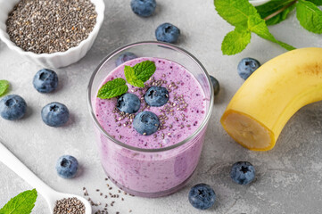 Smoothie with blueberries, banana, chia seeds and yogurt in a glass on a gray concrete background....