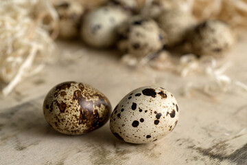 Close up of two spotted quail eggs on a wooden surface surrounded by straw