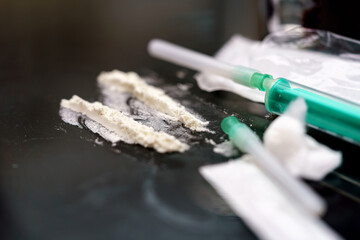 Syringes filled with liquids and powdered substances are placed on a reflective surface. The...