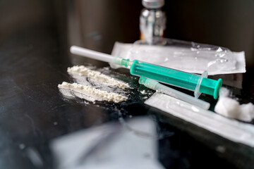 Syringes filled with liquids and powdered substances are placed on a reflective surface. The...