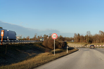 Speed limit sign on highway during clear day with vehicles approaching in the distance