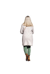 Femme de 60 ans vue de dos, marchant en automne avec un manteau long, pantalon vert et bottines, cheveux blonds mi-longs