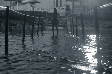 Silhouette of young woman with dark hair stands in dimly lit water passage. Reflective water...
