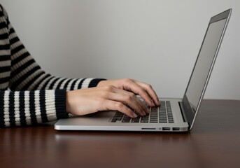 Hands typing on a laptop computer at a desk, working or studying