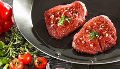 Raw seasoned pieces of raw meat, duck breast prepared for cooking, placed on a kitchen table surrounded by fresh ingredients and herbs  – healthy cooking and lifestyle concept. 