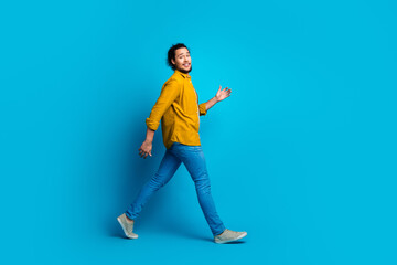 Stylish young man walking confidently against a bright blue background, showcasing modern fashion...
