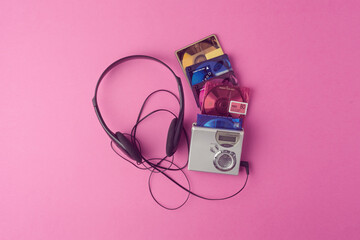 Silver minidisc player, black headphones, and colorful discs scattered on pink background revive playful and carefree 90s music nostalgia.