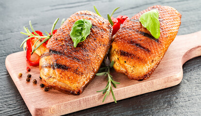 Seasoned pieces of grilled meat placed on a kitchen table surrounded by fresh ingredients, vegetables and herbs. Healthy eating, home cooking, food blogs and conscious food preparation concept.