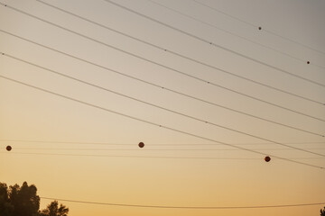 High-voltage power lines with red marker balls silhouetted against a clear sunset sky in Portugal. Captured to highlight infrastructure safety and visual contrast at dusk.