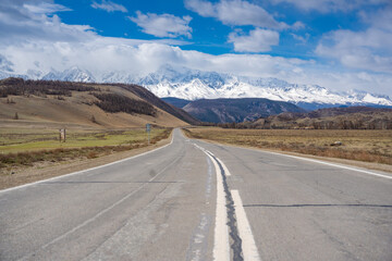 Naklejka premium Asphalt road leading to snow-covered Akturu ridge in Kurai steppe valley Altai, Russia