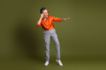 Middle aged woman in casual stylish attire striking a playful pose against a solid khaki green...