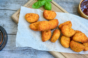 
 Crispy oven baked  chicken nuggets and  barbeque sauce . Breaded chicken fillets  with chilly peppers and fresh basi on wooden rustic background