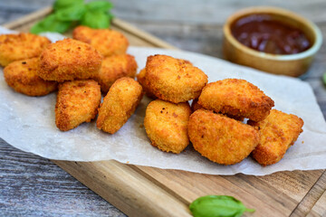 
 Crispy oven baked  chicken nuggets and  barbeque sauce . Breaded chicken fillets  with chilly peppers and fresh basi on wooden rustic background