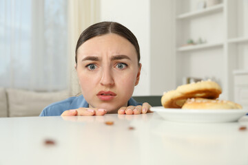 Shocked young woman looking at cockroaches and pretzels on white table indoors. Pest problem