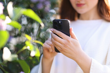Woman using plant recognition application on smartphone outdoors, selective focus