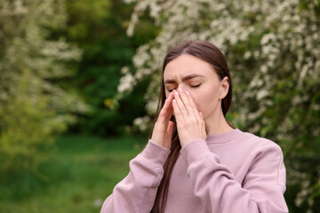 Woman suffering from seasonal pollen allergy near blossoming shrub on spring day, space for text