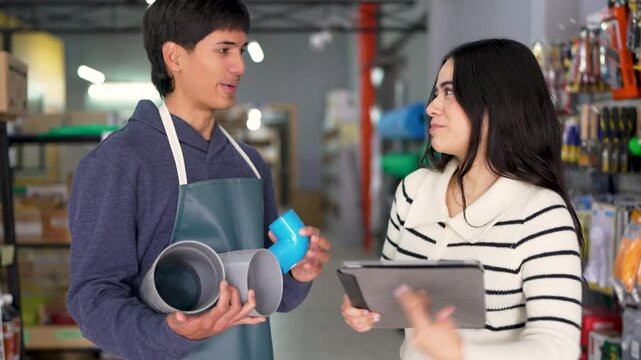 Shop assistant showing different plumbing pipes to a saleswoman in a hardware store