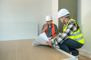 Two male construction workers wea helmets and safety vests discussing blueprints in an indoor...