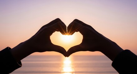 Hands forming a heart shape silhouetted against a beautiful sunset over the ocean