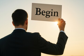 A businessman holds a sign labeled Begin as sunlight flares behind symbolizing strategy and decision-making at the start new business growth